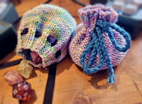 A photograph of two hand-knitted dice bags of a simple design, one tied shut and the other with a few dice spilling out.